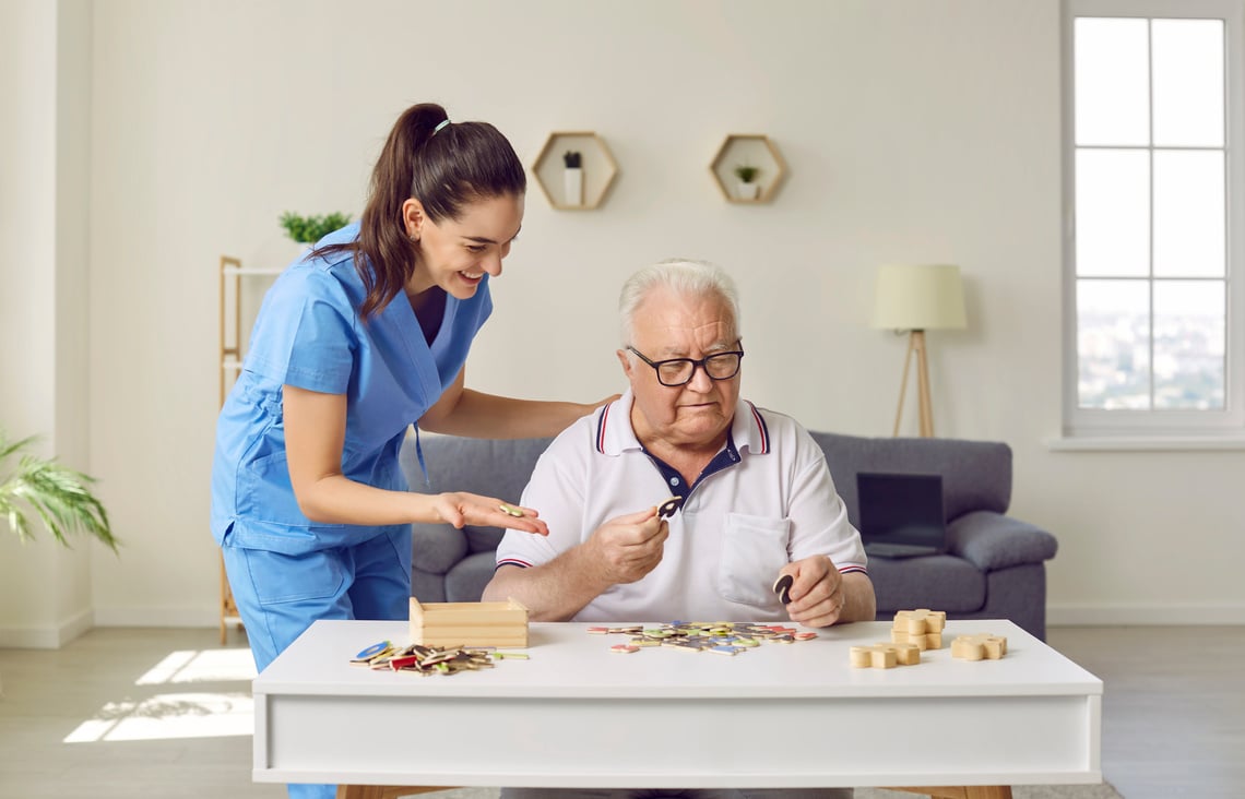 Nurse in Retirement Home Helping Senior Man with Alzheimer's Disease with Puzzles